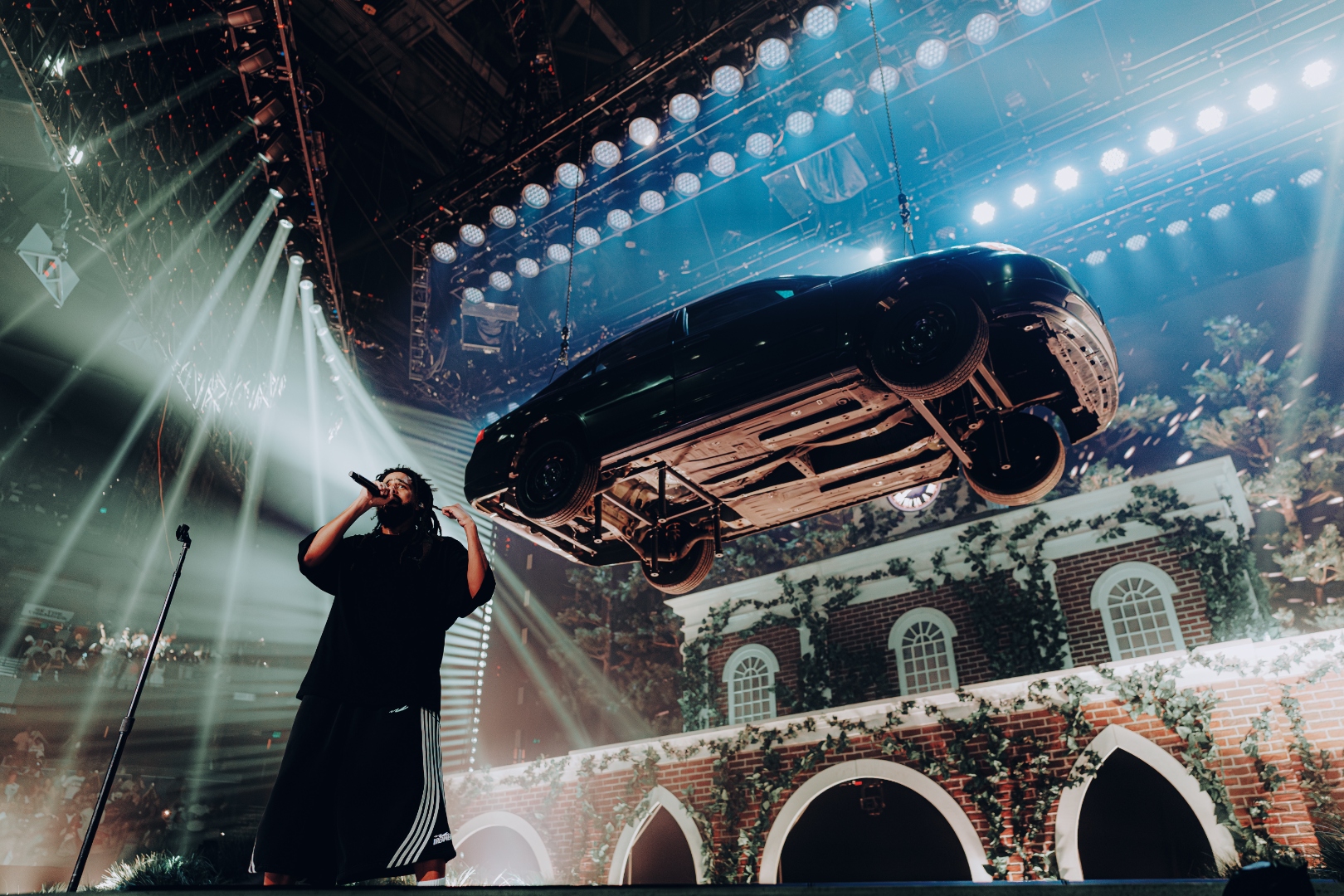 J. Cole on stage in Tampa with a suspended car and brick facade set piece